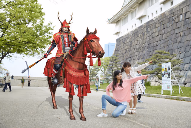 A tourism AR app example: AR samurai on horseback appearing in front of Osaka Castle while visitors take photos